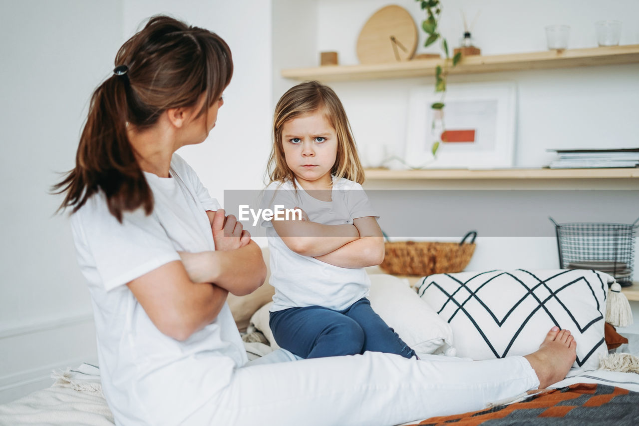 Woman looking at daughter sitting with arms crossed