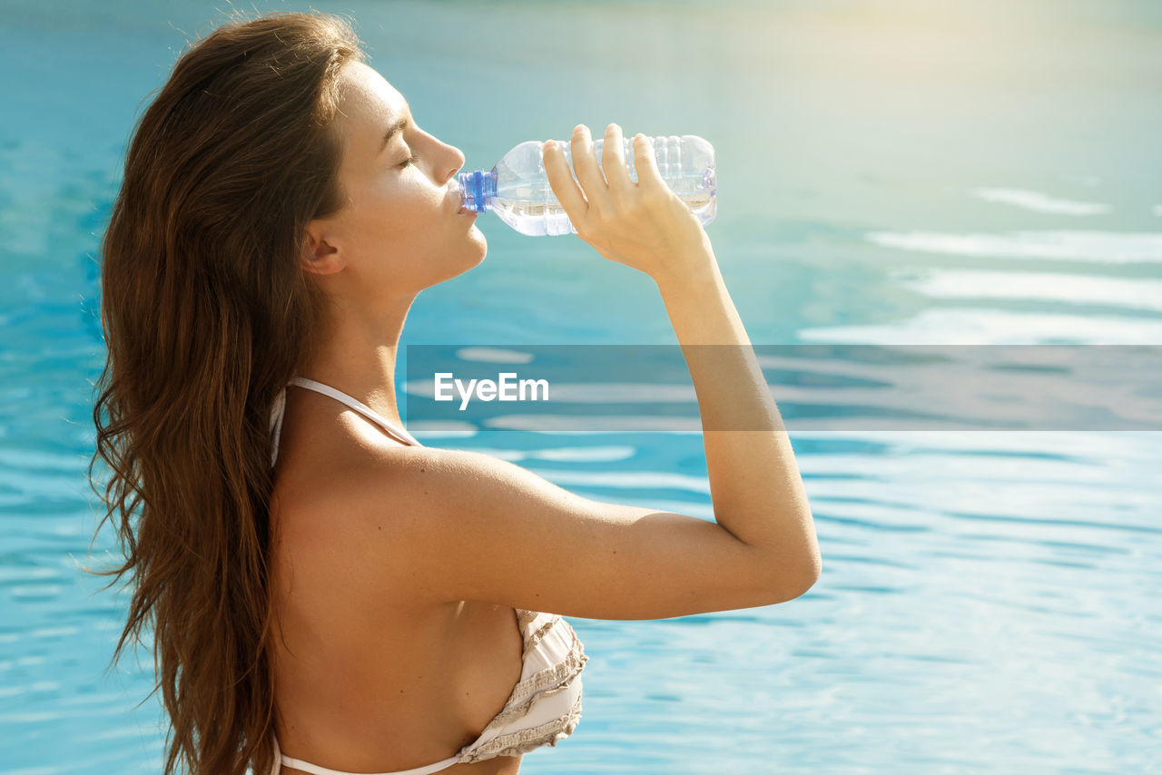 Side view of beautiful woman drinking water in swimming pool