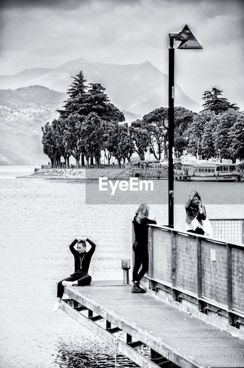 PEOPLE SITTING BY RAILING AGAINST MOUNTAIN