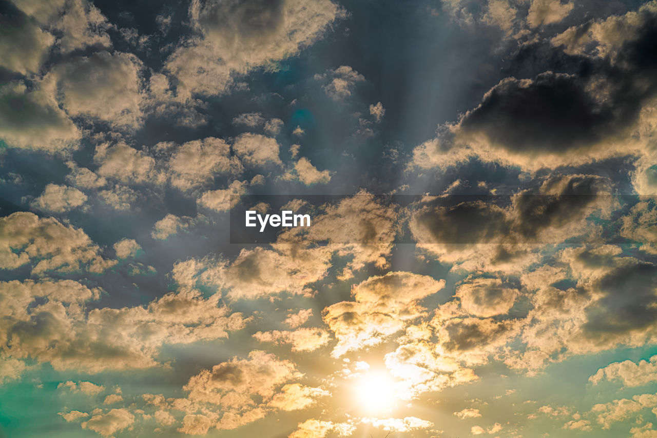 LOW ANGLE VIEW OF SUN STREAMING THROUGH CLOUDS IN SKY