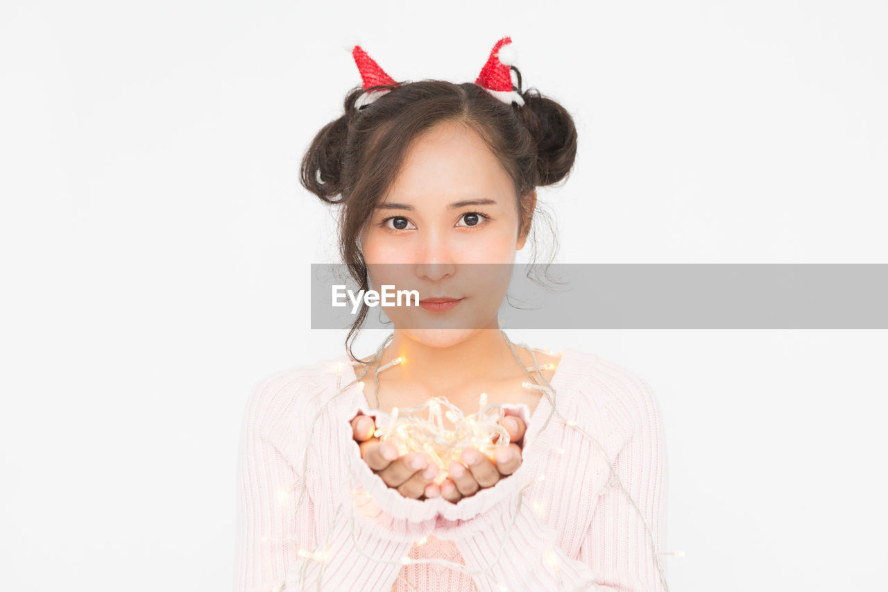 Asian woman wearing santa hat and wearing pink sweater holding christmas lights on white background