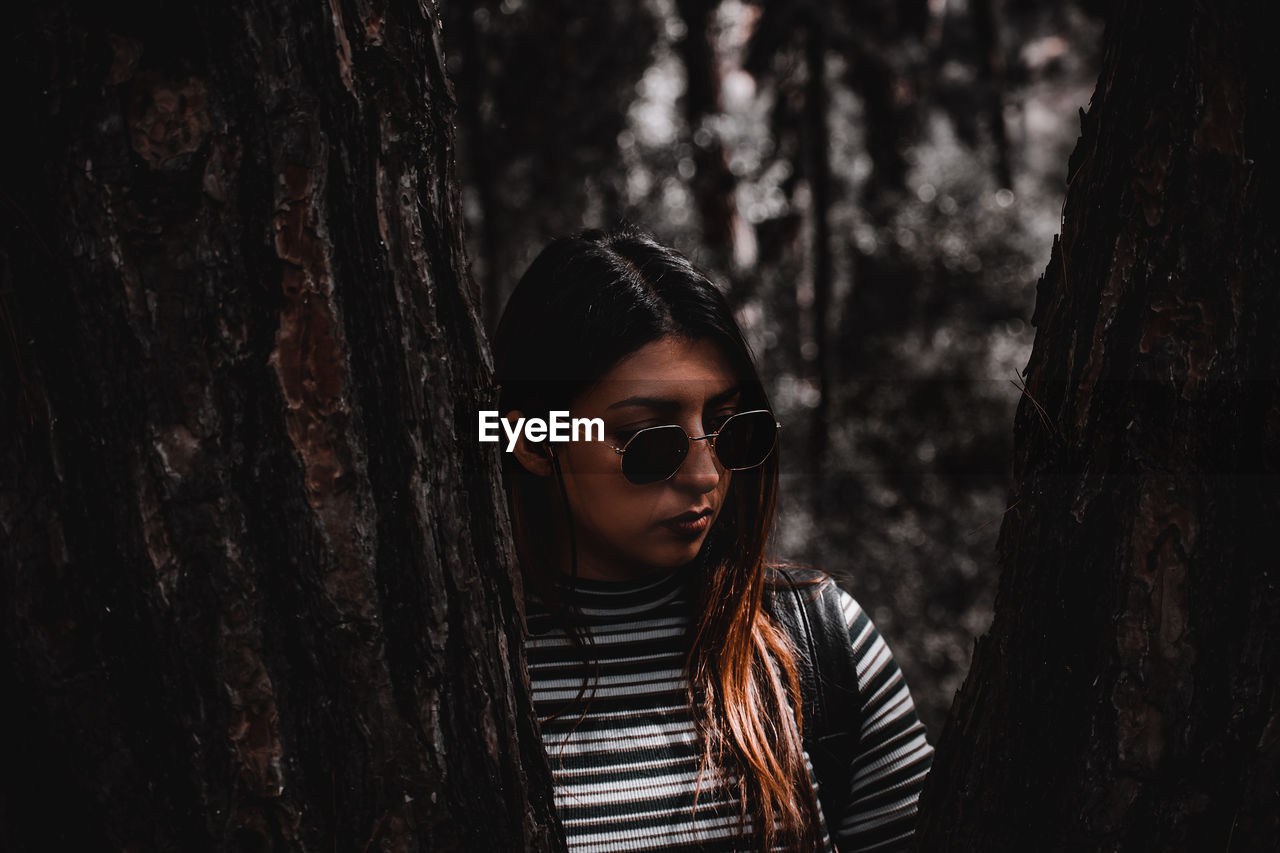 Portrait of beautiful young woman standing by tree trunk