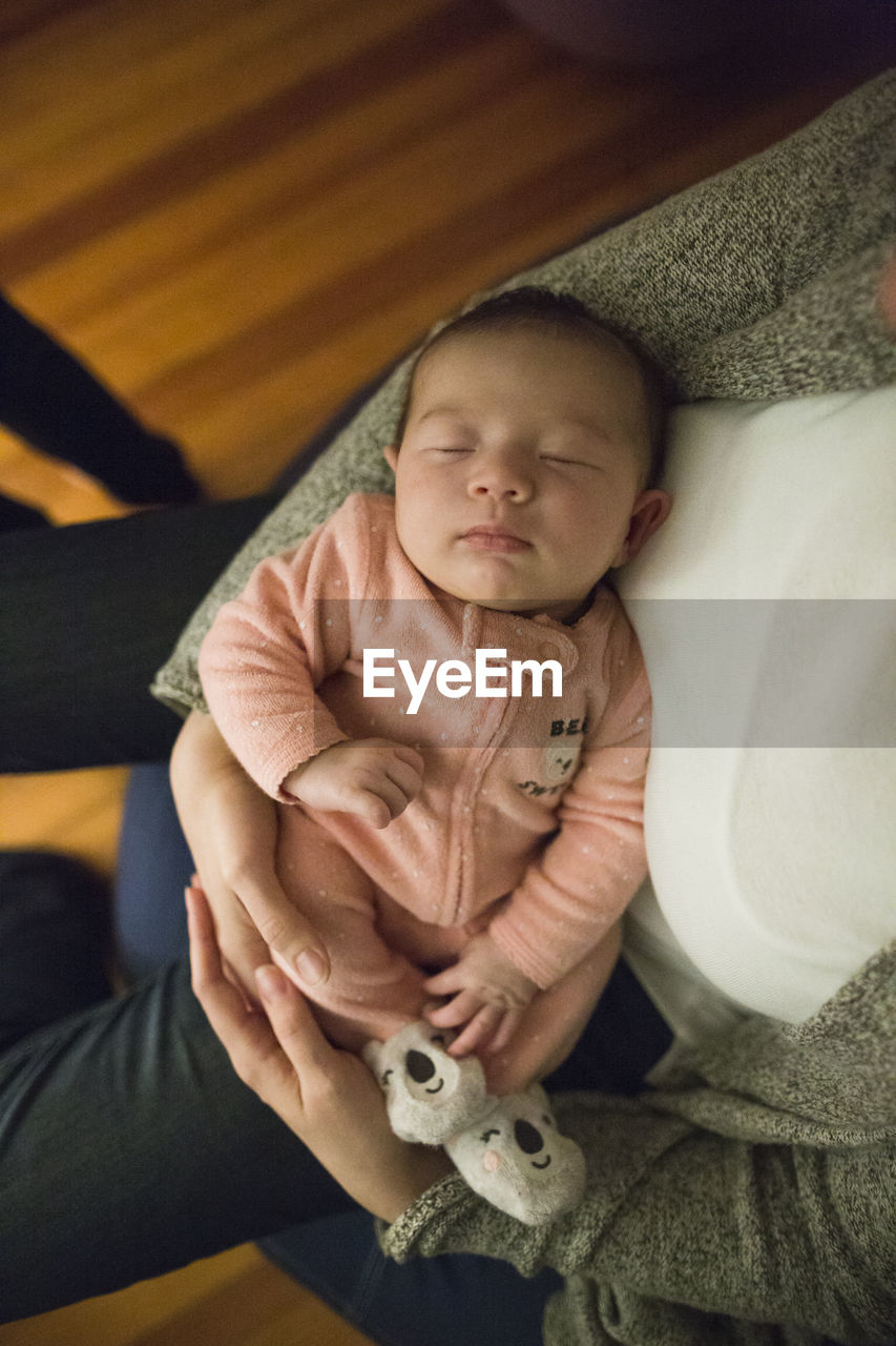 Newborn baby girl sleeps peacefully in mother's arms indoors