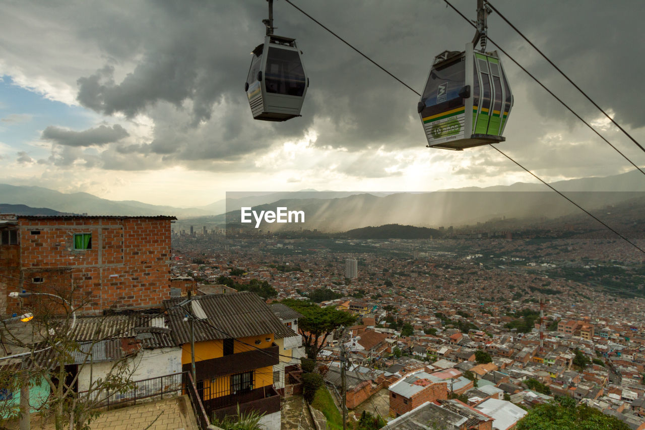 Overhead cable cars over cityscape against cloudy sky