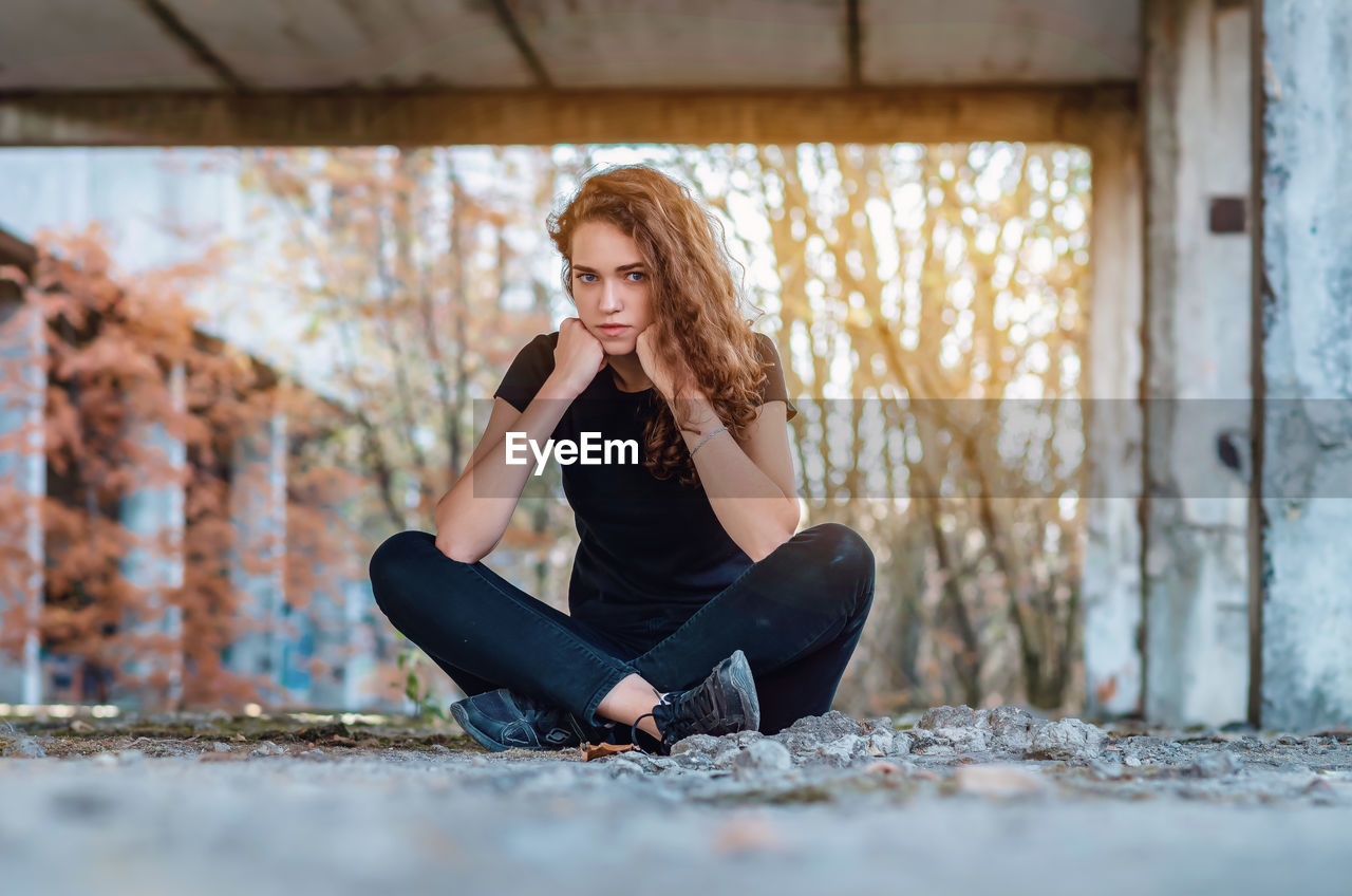 Teenage girl sits cross-legged, supports head with fists, legs crossed. evil look of blue eyes.