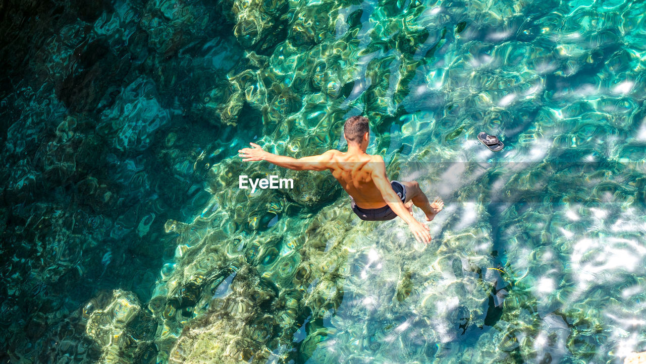 HIGH ANGLE VIEW OF SHIRTLESS MAN SWIMMING IN SEA