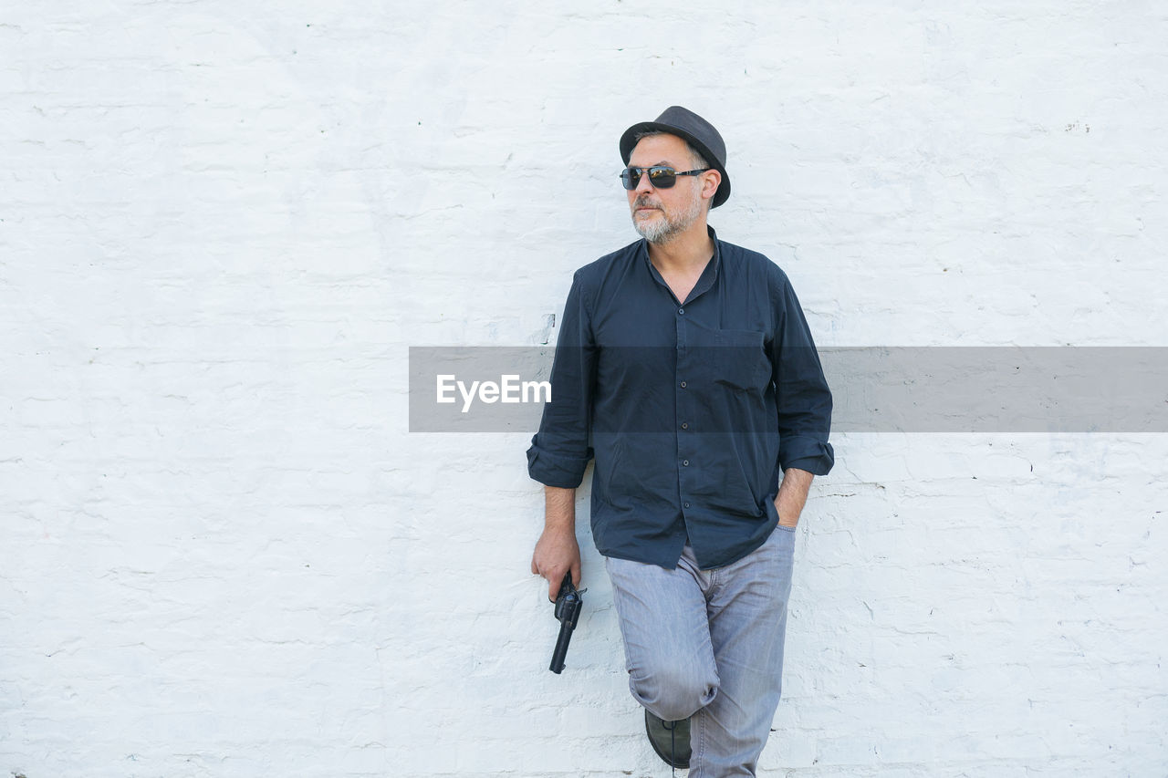 Man wearing sunglasses holding gun against white wall