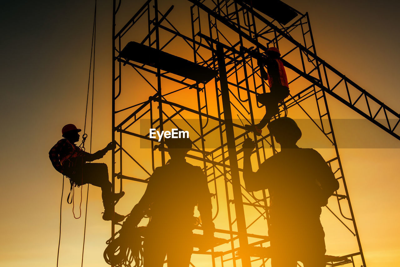 LOW ANGLE VIEW OF SILHOUETTE PEOPLE WORKING AGAINST SKY