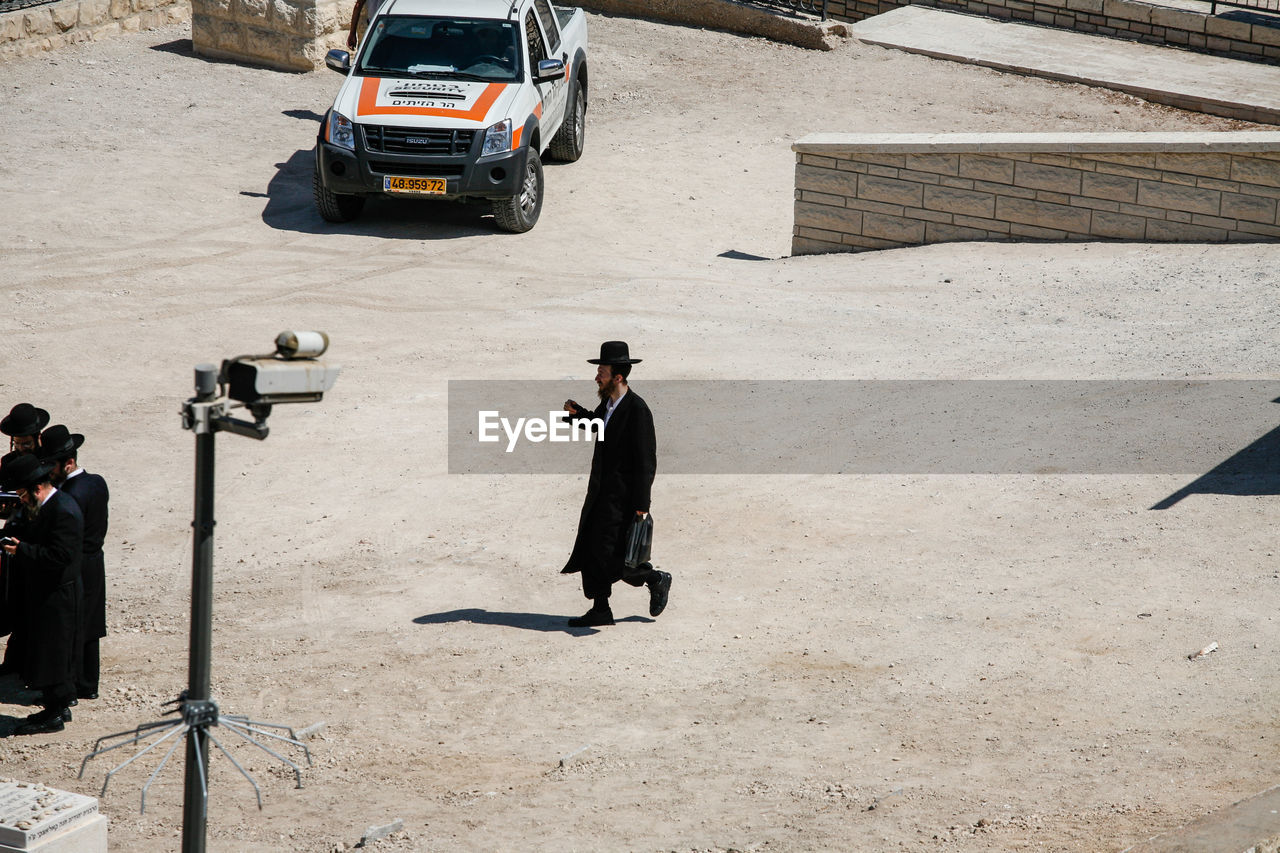 HIGH ANGLE VIEW OF MEN STANDING ON ROAD