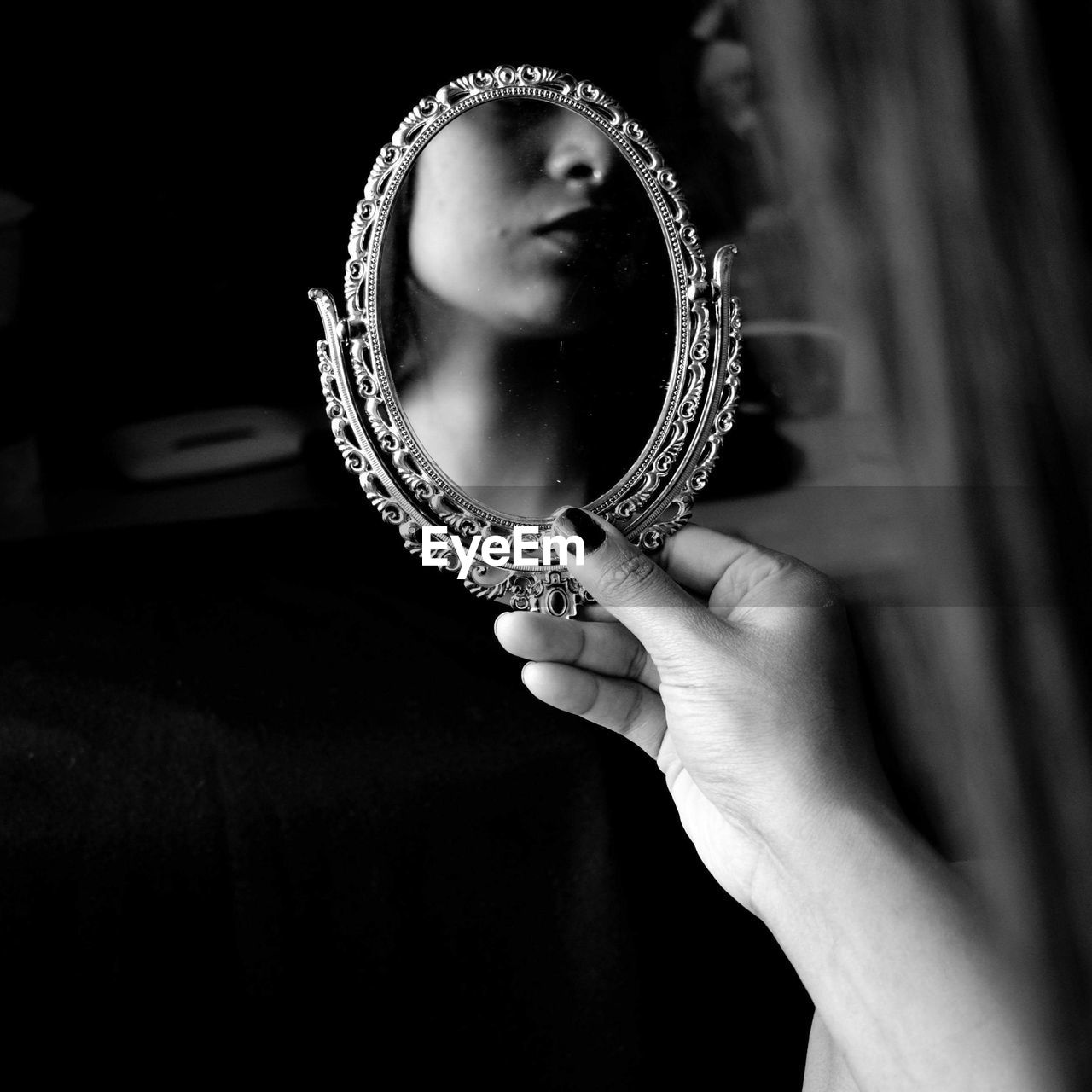 Cropped hand of woman holding mirror with reflection at home