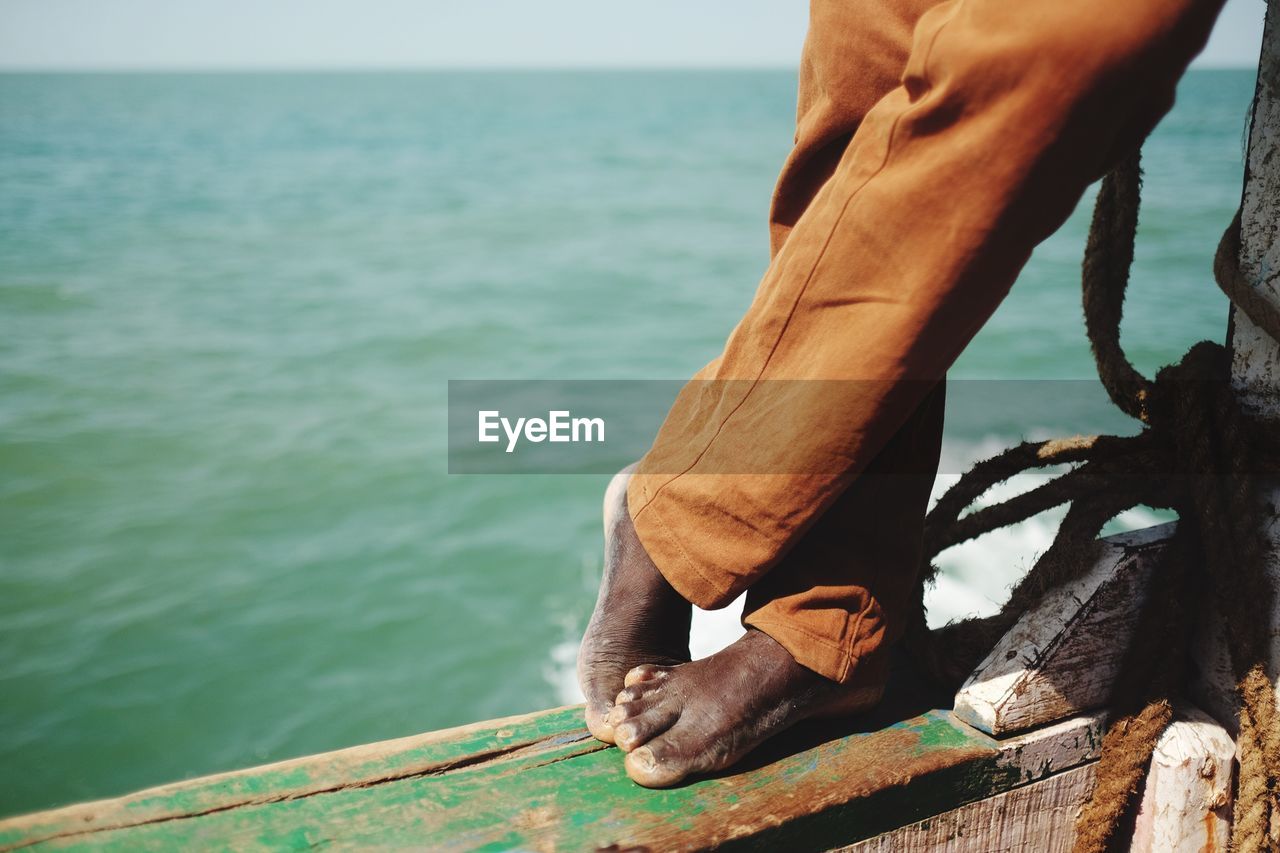 Low section of man standing on boat sailing in sea