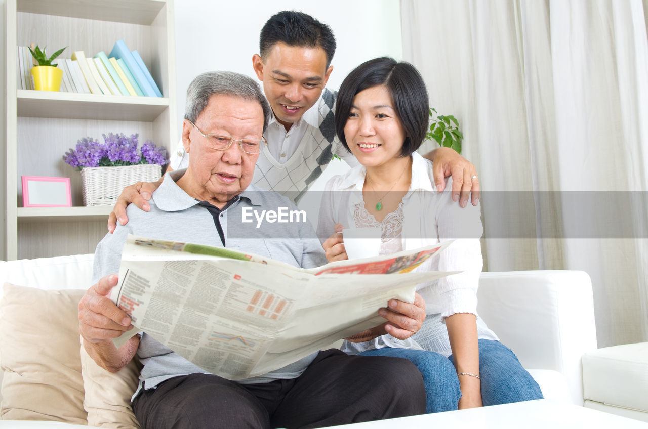 Happy family reading newspaper while sitting on sofa at home