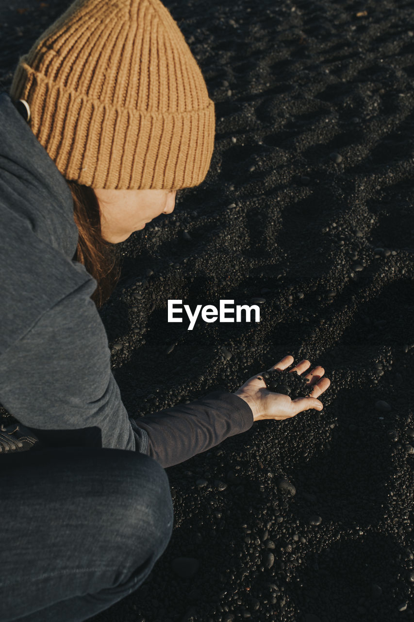 Woman picking up black sand on volcanic beach