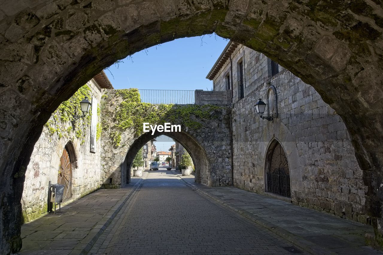 ARCH BRIDGE AMIDST BUILDINGS AGAINST SKY SEEN THROUGH ARCHWAY