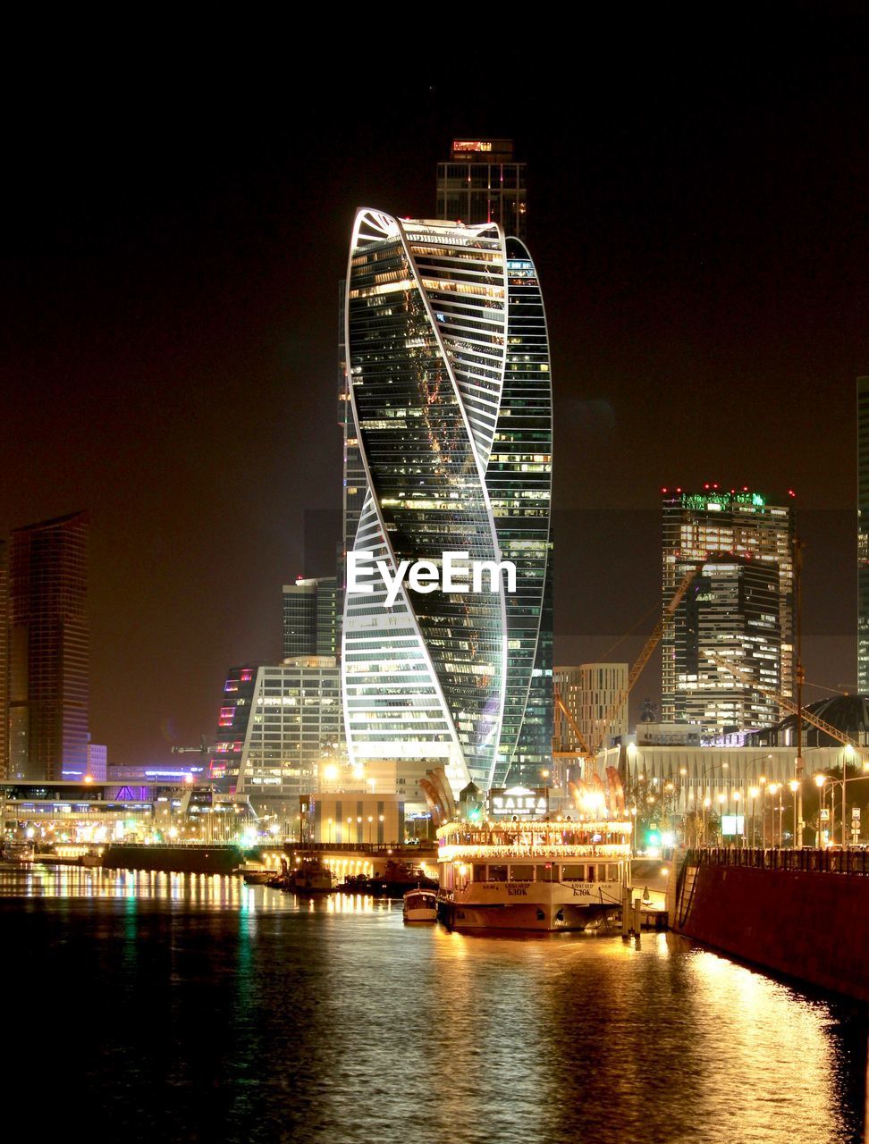 ILLUMINATED BUILDINGS BY RIVER AT NIGHT