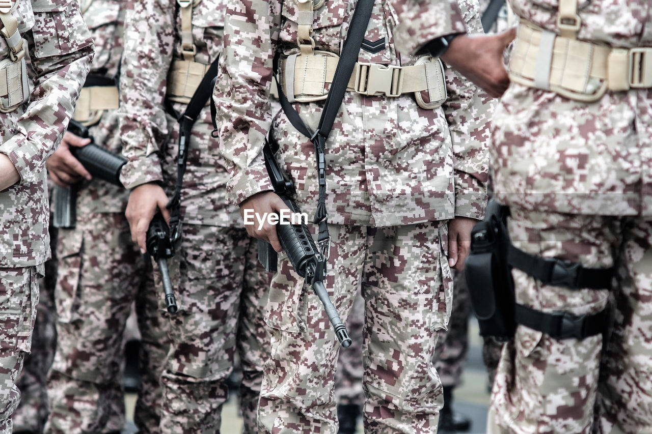 Midsection of army soldiers with machine guns standing outdoors