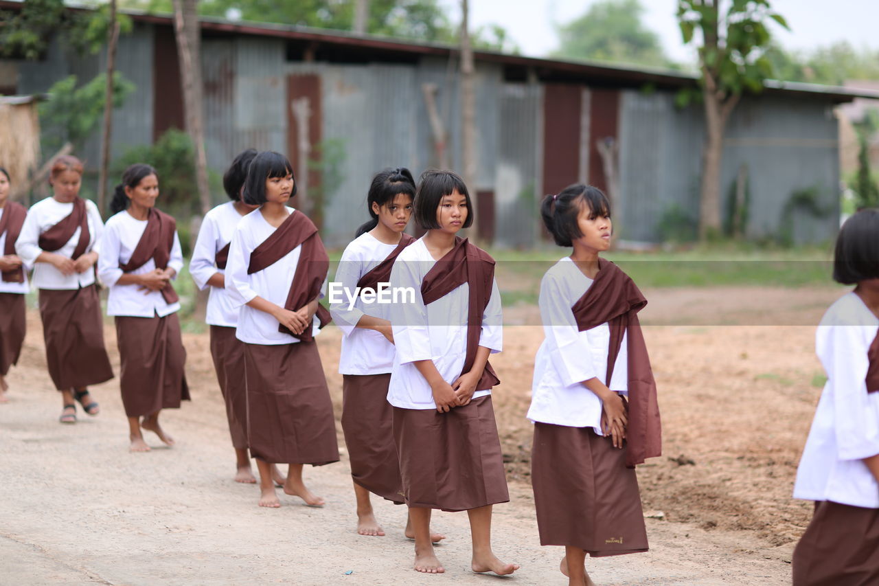 GROUP OF PEOPLE WALKING IN FRONT OF TWO MEN