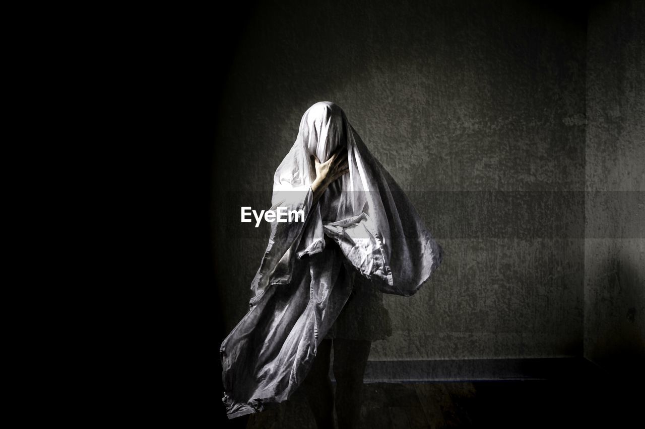 Obscured face of mature woman wearing textile against wall at abandoned place