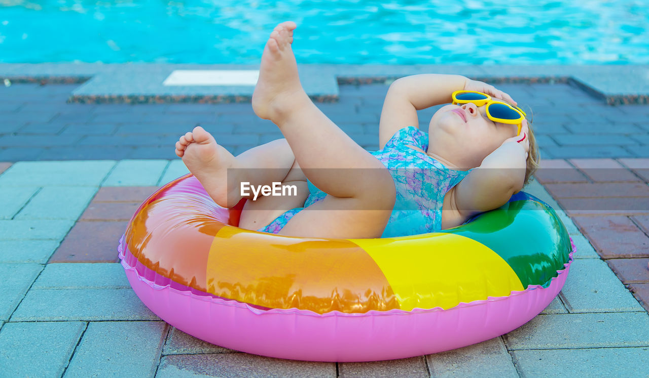 Cute baby lying on inflatable ring by swimming pool