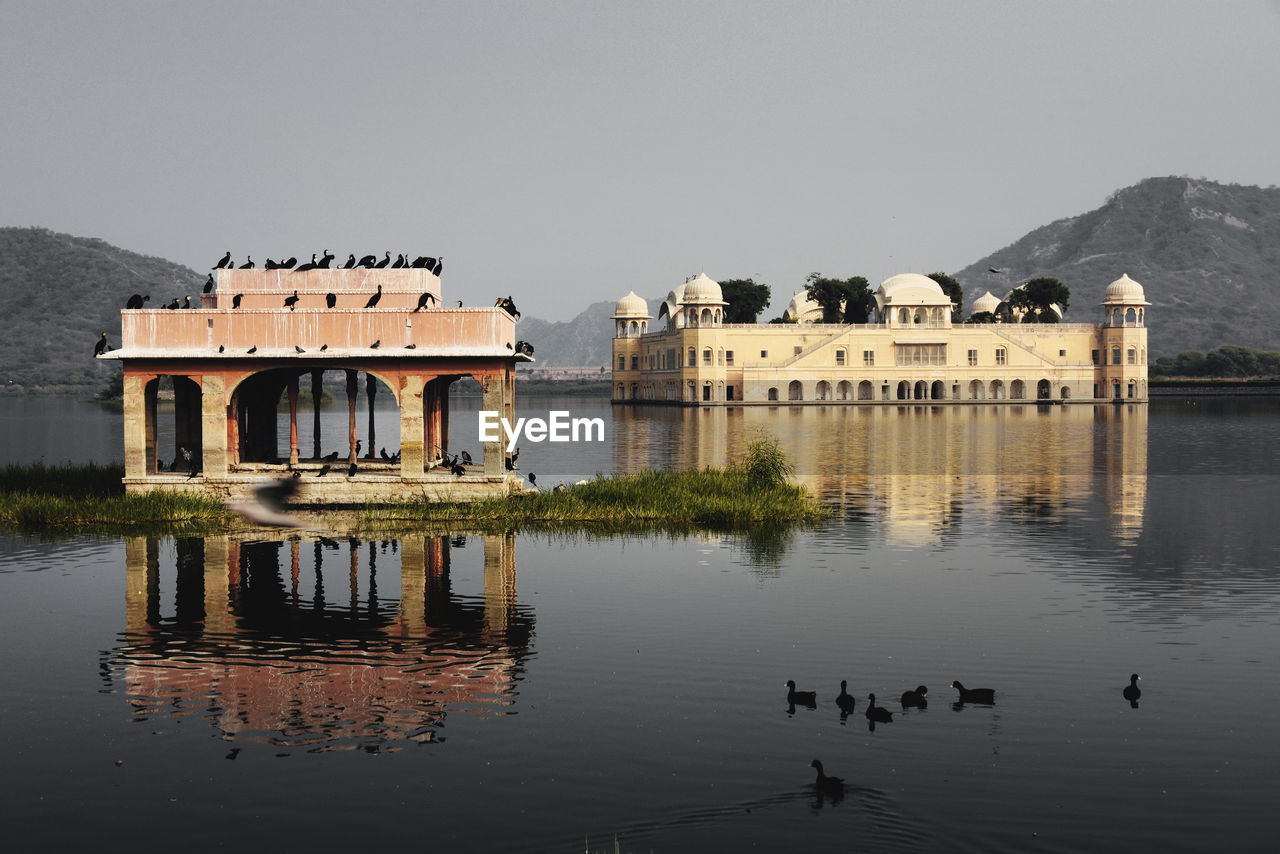 Birds and built structures in lake against clear sky