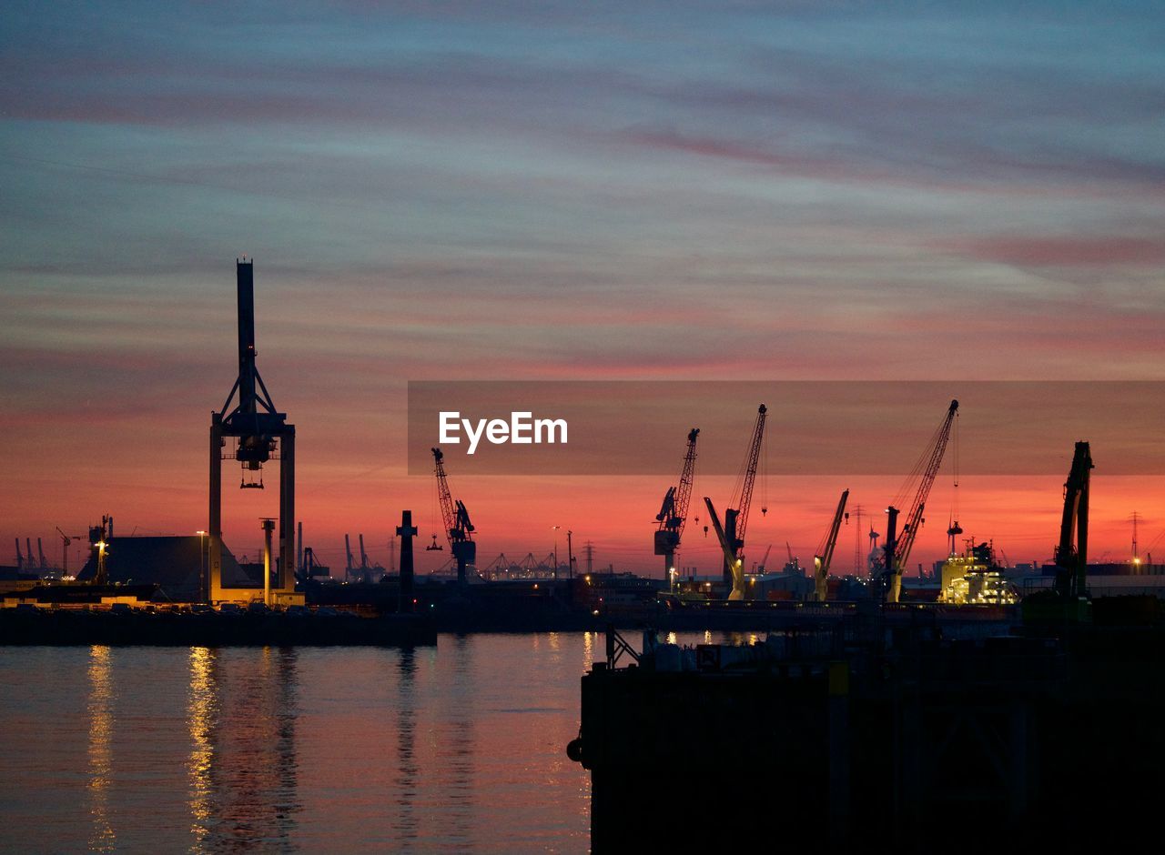 CRANES AT HARBOR AGAINST SKY DURING SUNSET