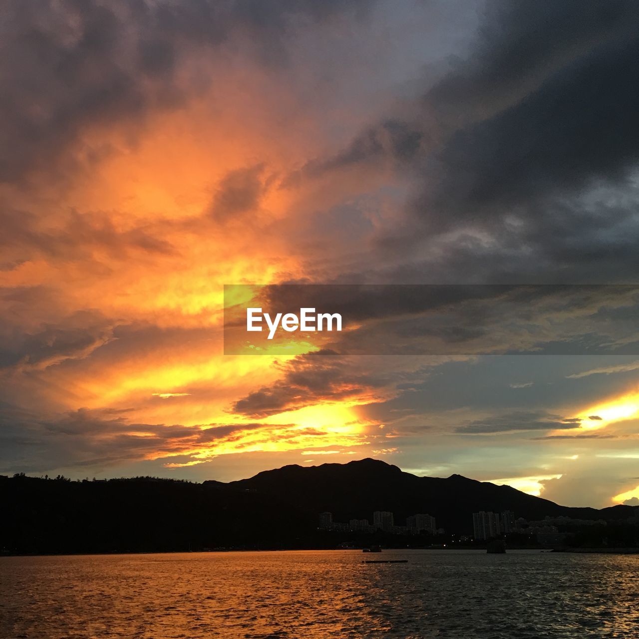 SCENIC VIEW OF LAKE BY SILHOUETTE MOUNTAINS AGAINST DRAMATIC SKY