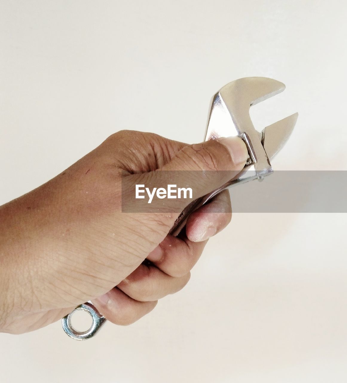 Close-up of hand holding wrench against white background