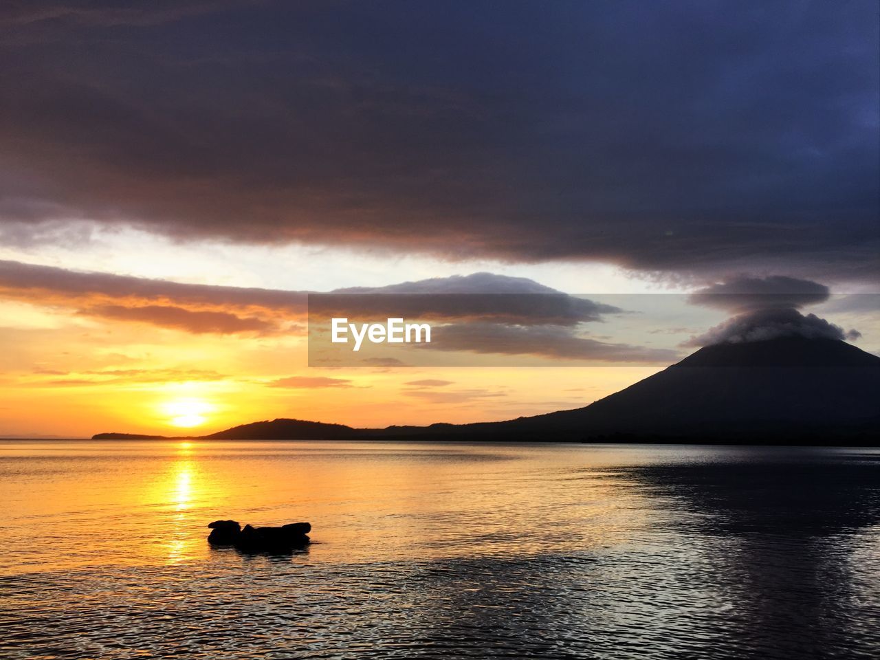 Scenic view of lake against cloudy sky during sunset