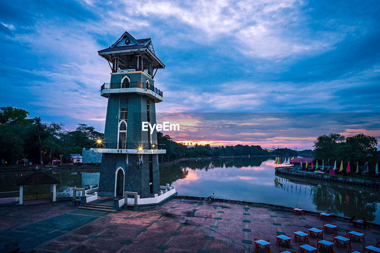 TRADITIONAL BUILDING BY LAKE AGAINST SKY DURING SUNSET