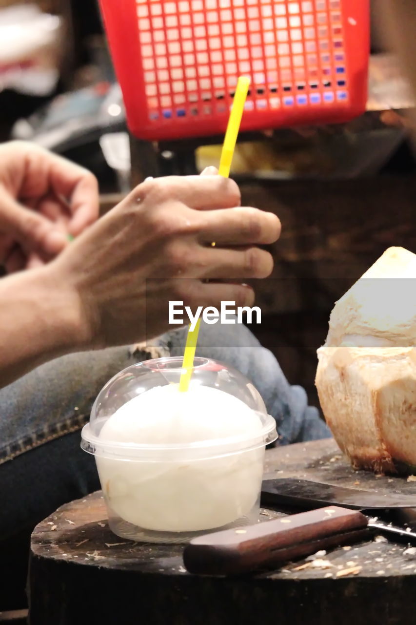 MIDSECTION OF PERSON HOLDING ICE CREAM WITH GLASS OF TABLE