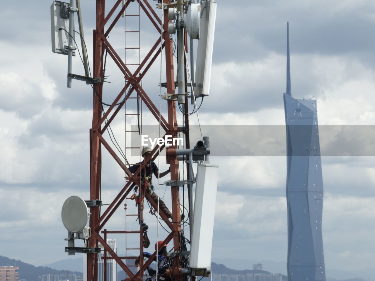 Man at work on telco tower with cityscape on barckground