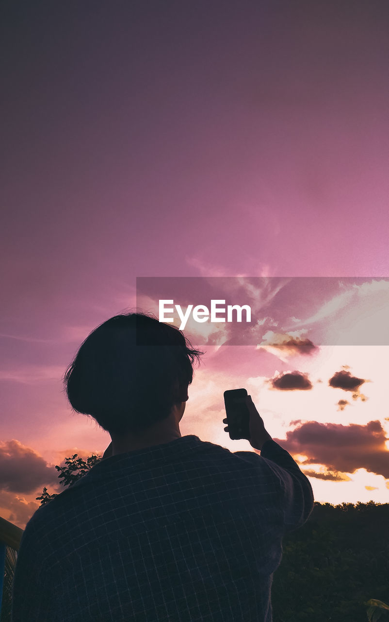 Rear view of silhouette man photographing against sky during sunset