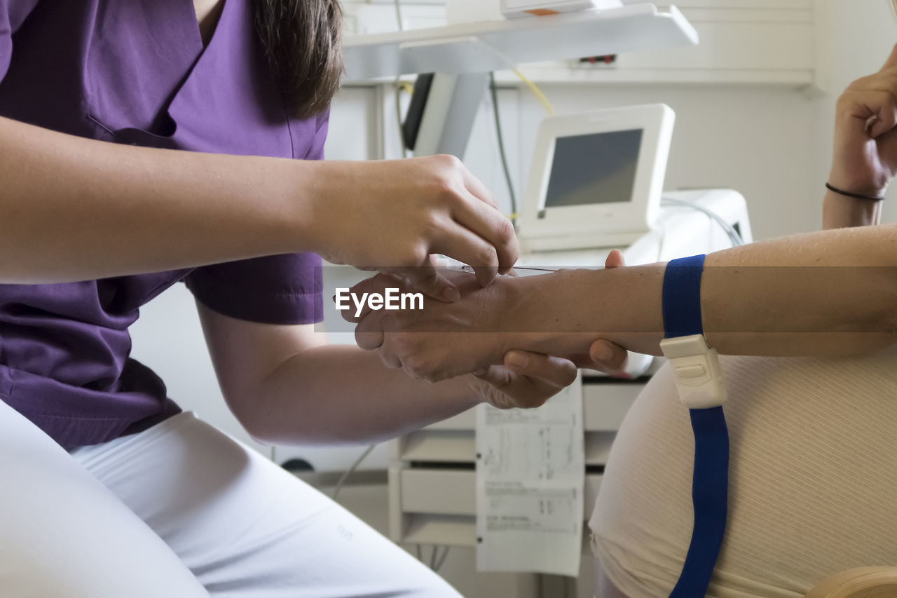 Midsection of nurse putting iv needle into patient hand at hospital