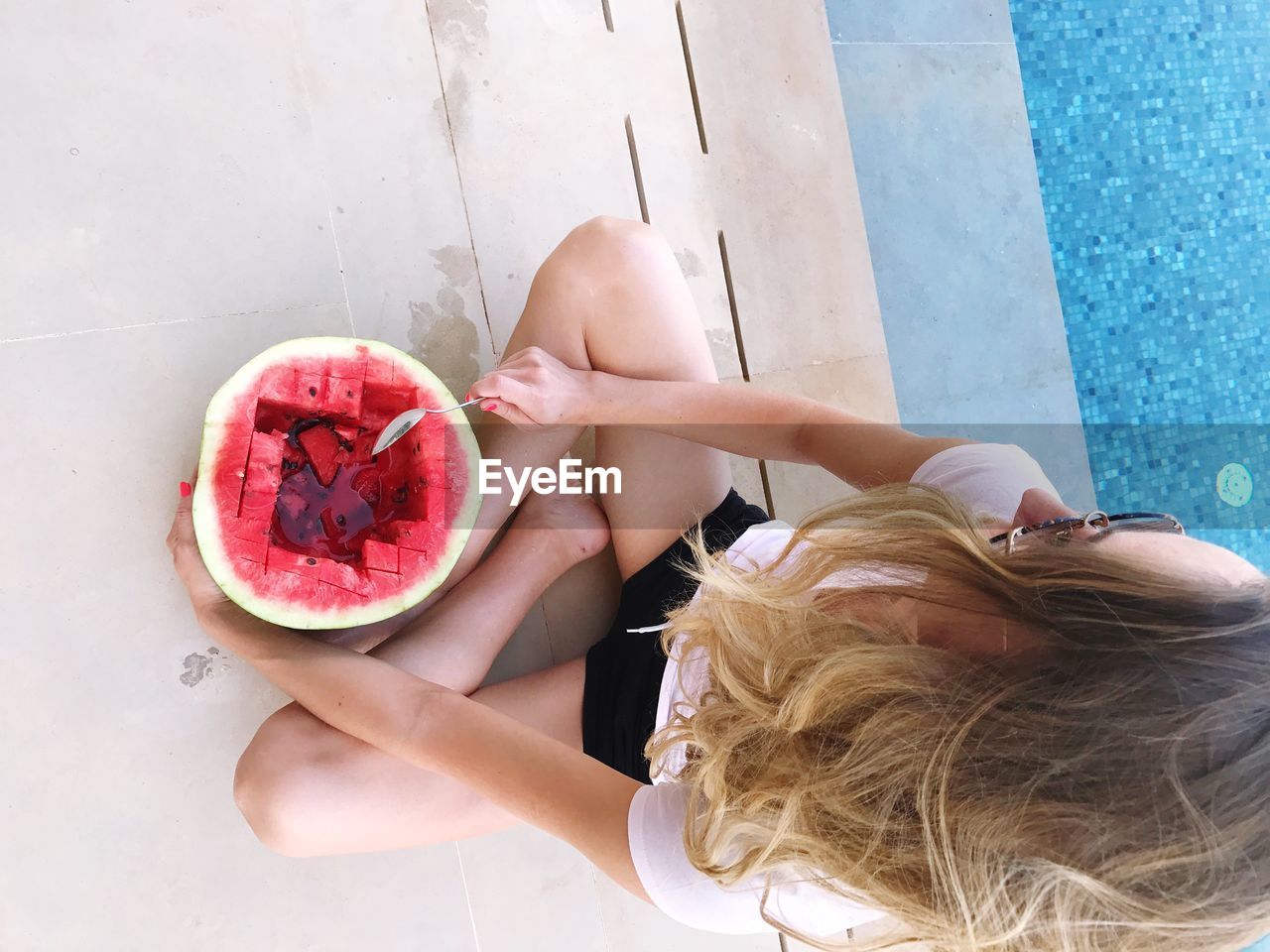 High angle view of mid adult woman having watermelon while sitting at poolside