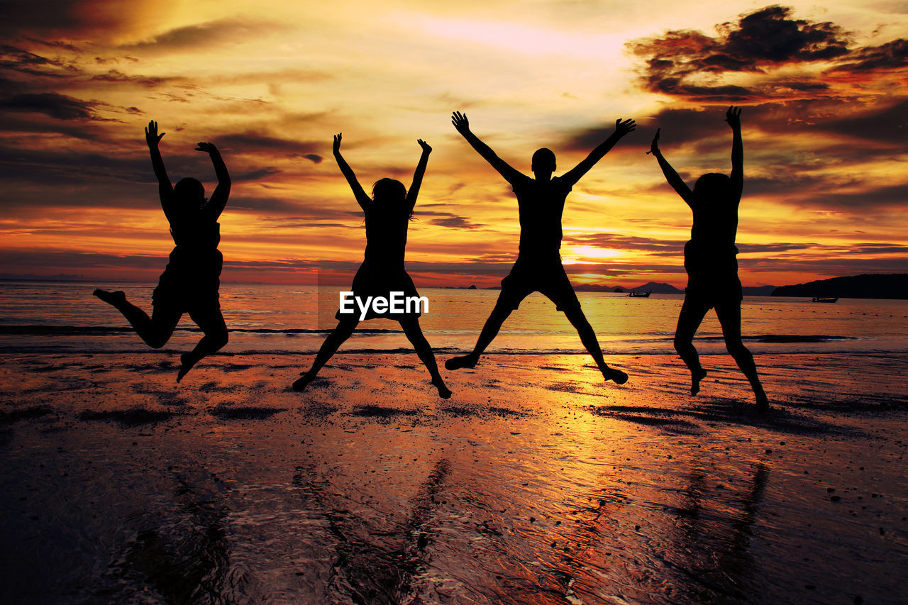 Silhouette friends jumping at beach during sunset