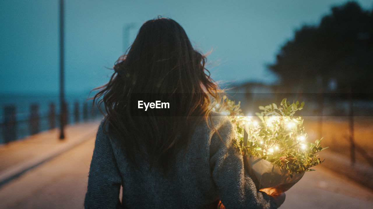 Young girl walks with a bouquet of plants and party lights in her hand