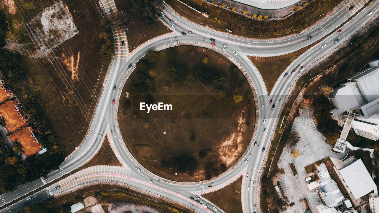 Top down aerial view of a traffic roundabout on a main road in an urban area.