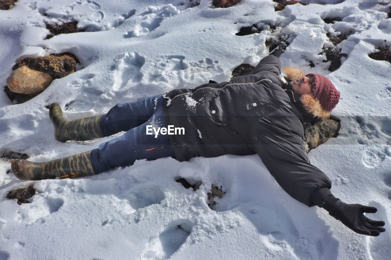 MAN LYING ON SNOW COVERED FIELD DURING WINTER