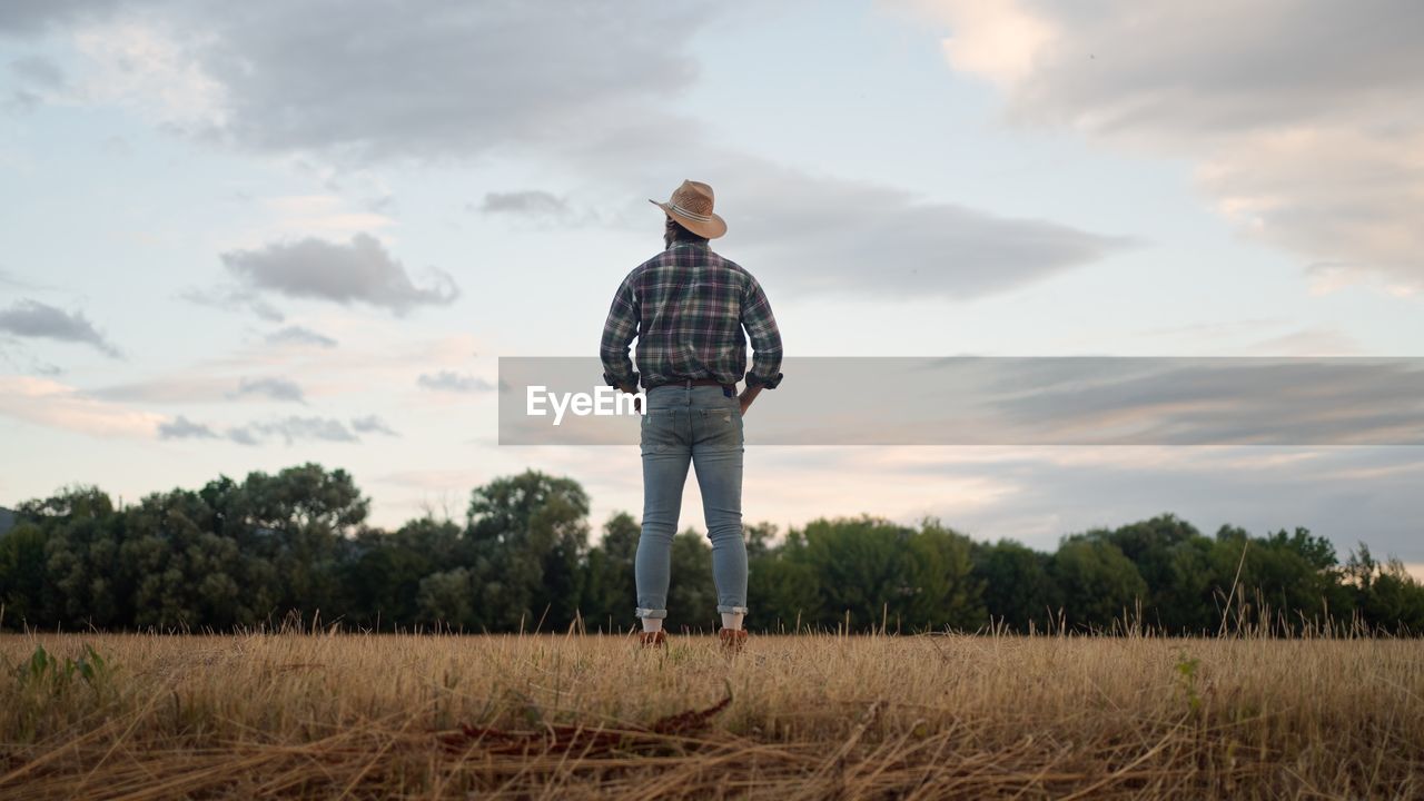 Rear shot of the farmer in the field looking at the cloudy sky