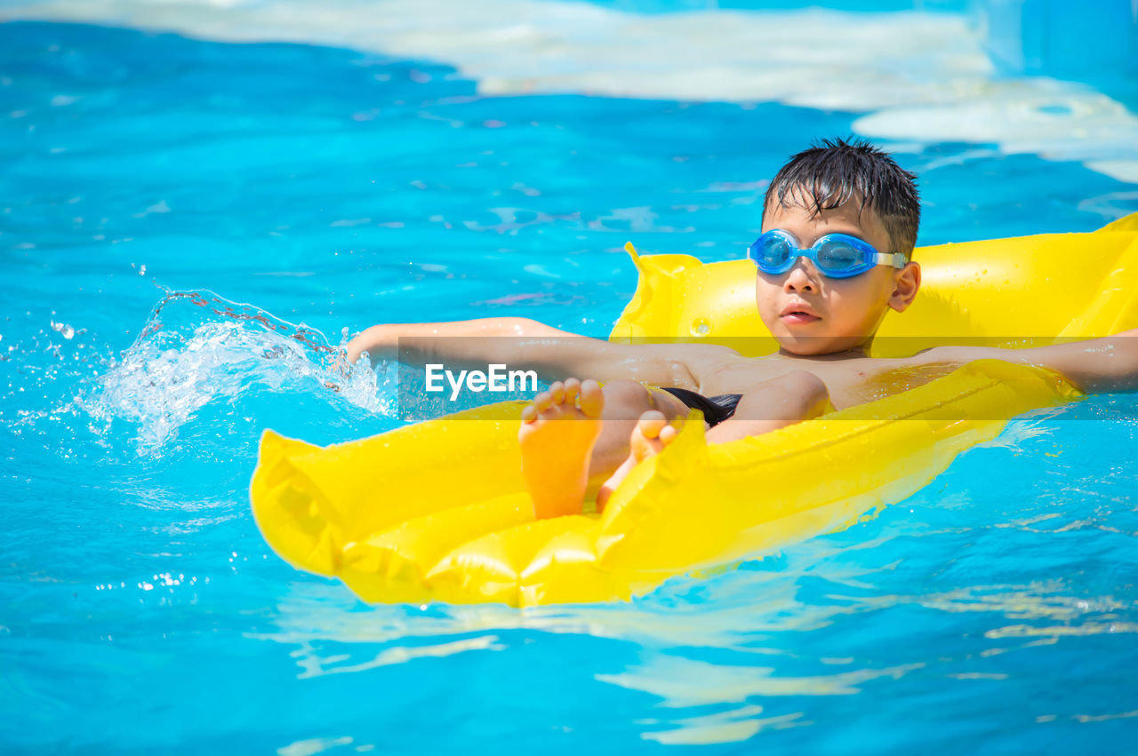 Boy swimming in pool on inflatable pool raft
