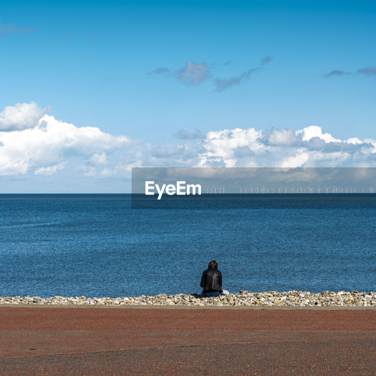 Rear view of woman sitting on beach against sky