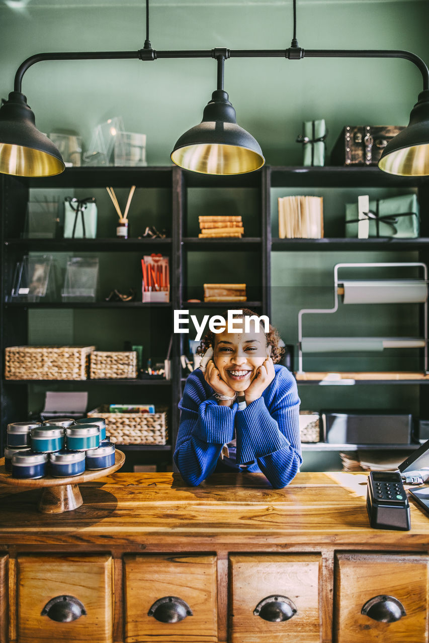 Portrait of happy woman leaning on desk at store