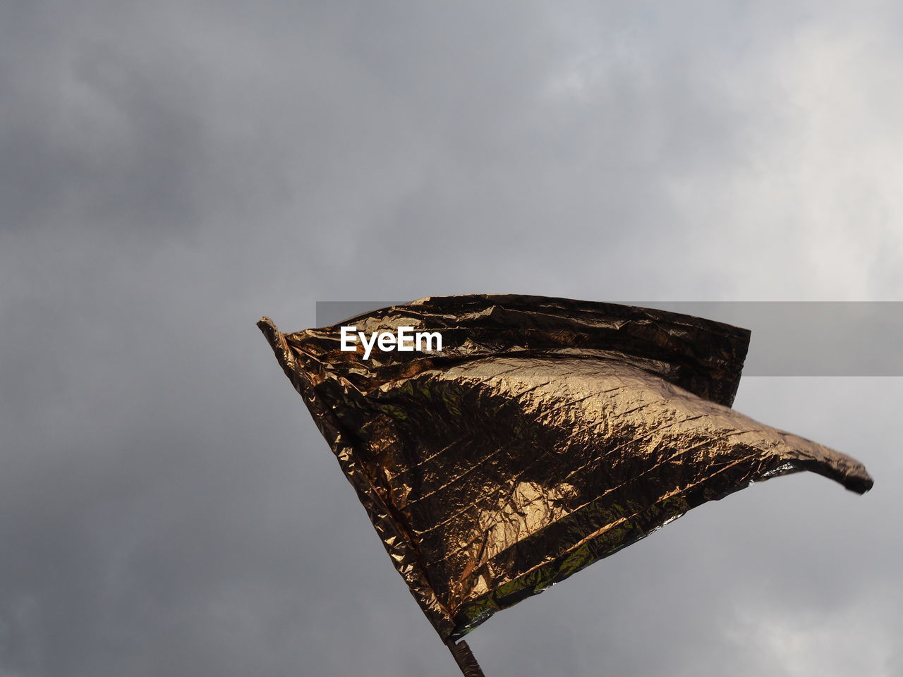 Low angle view of golden flag against cloudy sky