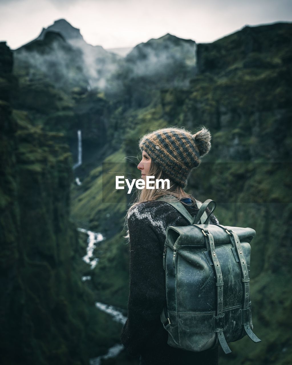 Woman looking away while standing against mountain and sky