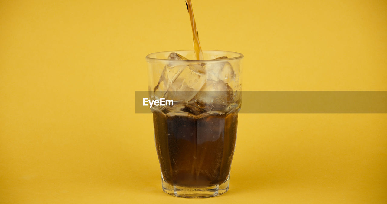 Glass with cold drink and ice against yellow background