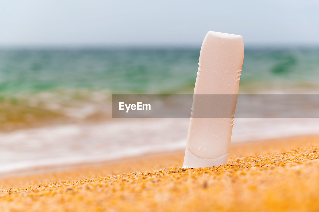 Bottle with sunscreen lotion on the beach, background of sea sky and waves, close-up. layout for