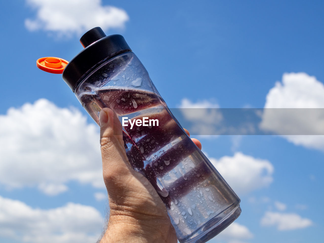 MIDSECTION OF PERSON HOLDING DRINK AGAINST SKY