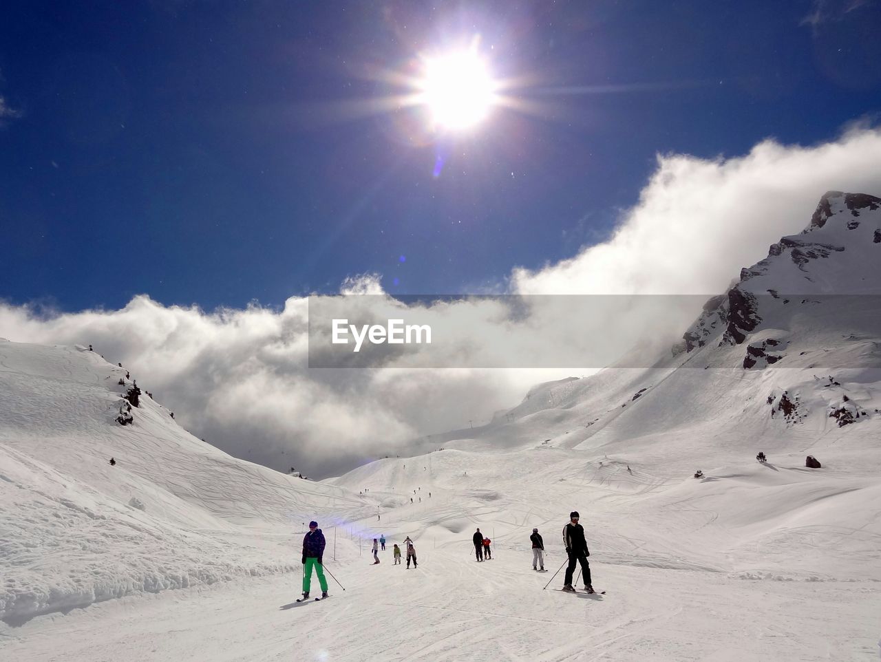 Low angle view of people skiing on snowcapped mountains on sunny day