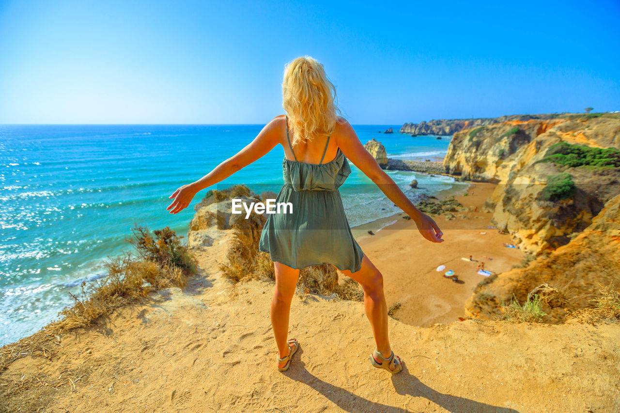 Rear view of woman standing on cliff against sea