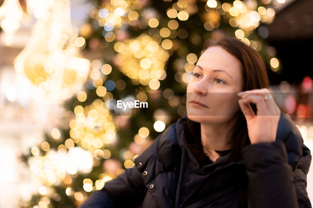 Portrait of a beautiful woman on the background of a christmas tree with bright lights garland